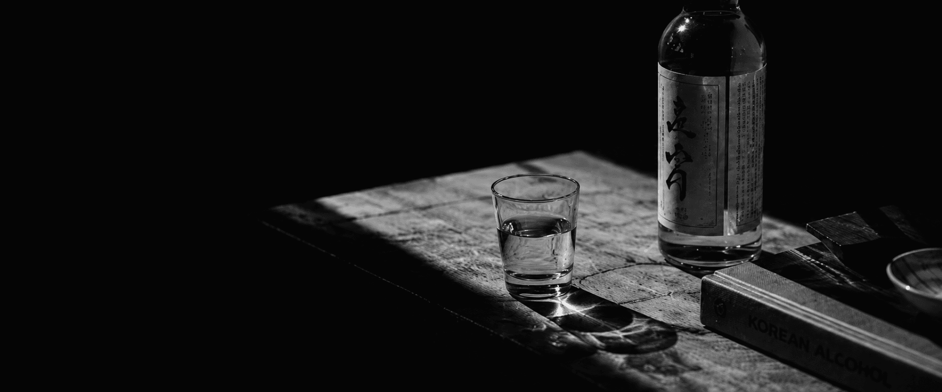 A bottle and glass of Korean alcohol on a dark wooden table